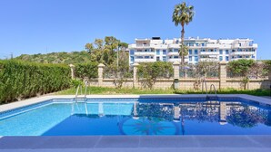 A swimming pool with a clear blue water feature, surrounded by a landscaped area with a palm tree and a multi-story building in the background. - Apartment 'Argia' with Sea View, Wi-Fi, and Air Conditioning (Algarrobo)