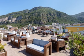 A rooftop terrace with wooden furniture, a dining area, and a view of a mountainous landscape. - Room 'Matrimoniale Mansardata' with Shared Terrace, Wi-Fi and Air Conditioning (Meta)