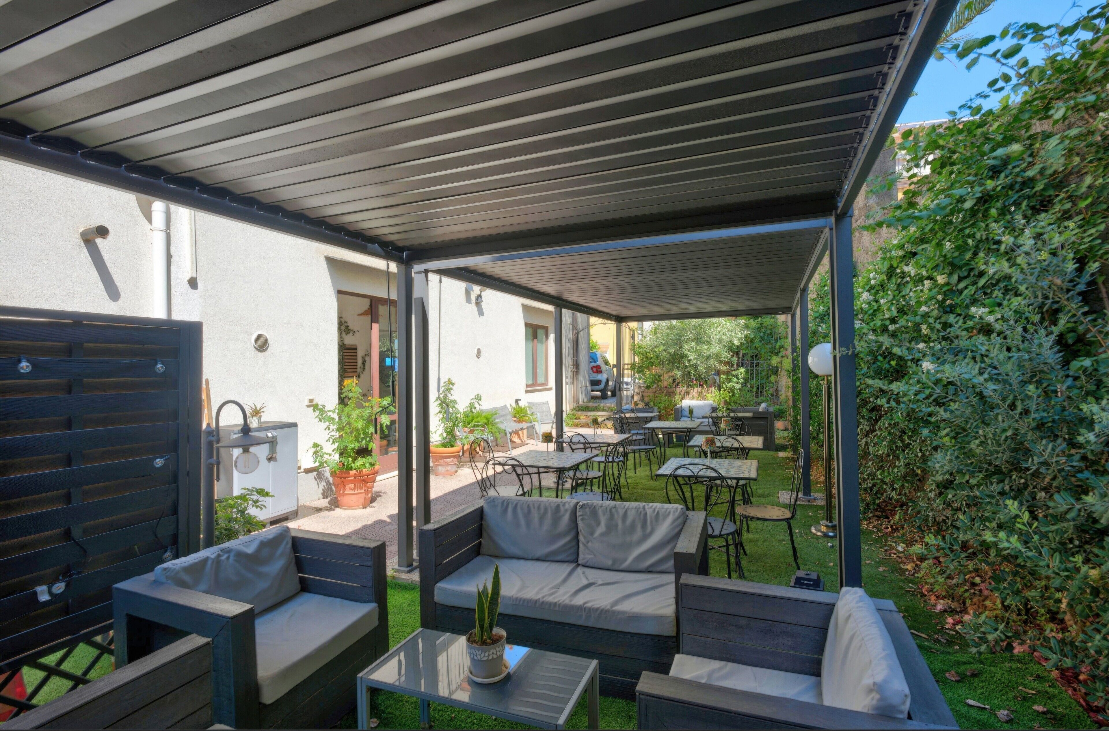 Eine einladende Terrassenanlage mit überdachtem Sitzbereich, Tischen und Topfpflanzen.