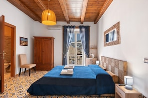 A bedroom with a bed, a chair, a wardrobe, a window with curtains, a lamp, and a view of the outside.