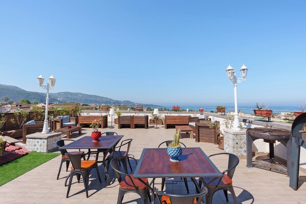 Eine Terrassenanlage im Freien mit Tischen und Stühlen, einer Sukkulenten-Dekoration und Blick aufs Meer.