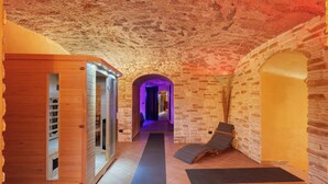 Un espace bien-être comprenant un sauna en bois, une salle de massage et un salon de détente offrant une vue sur les murs en pierre.