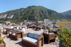 Terraço no telhado com móveis de madeira, área de refeições e vista para uma paisagem montanhosa.