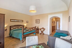 Quarto com cama de madeira, uma mesinha com uma planta, uma cadeira e luminária pendente.