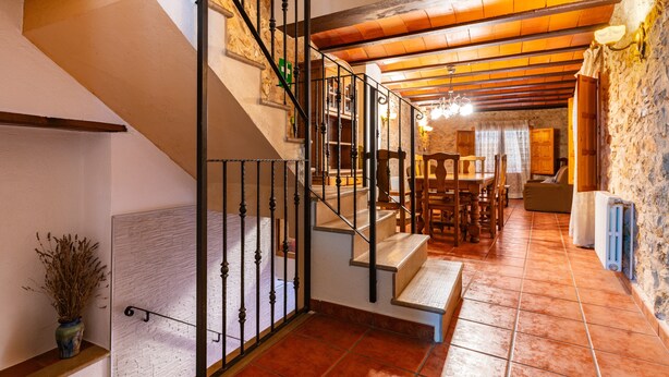 A staircase with a metal railing, a dining area with wooden furniture, and a stone wall. - Country House 'Virginia' with Mountain View and Balcony (Unknown)