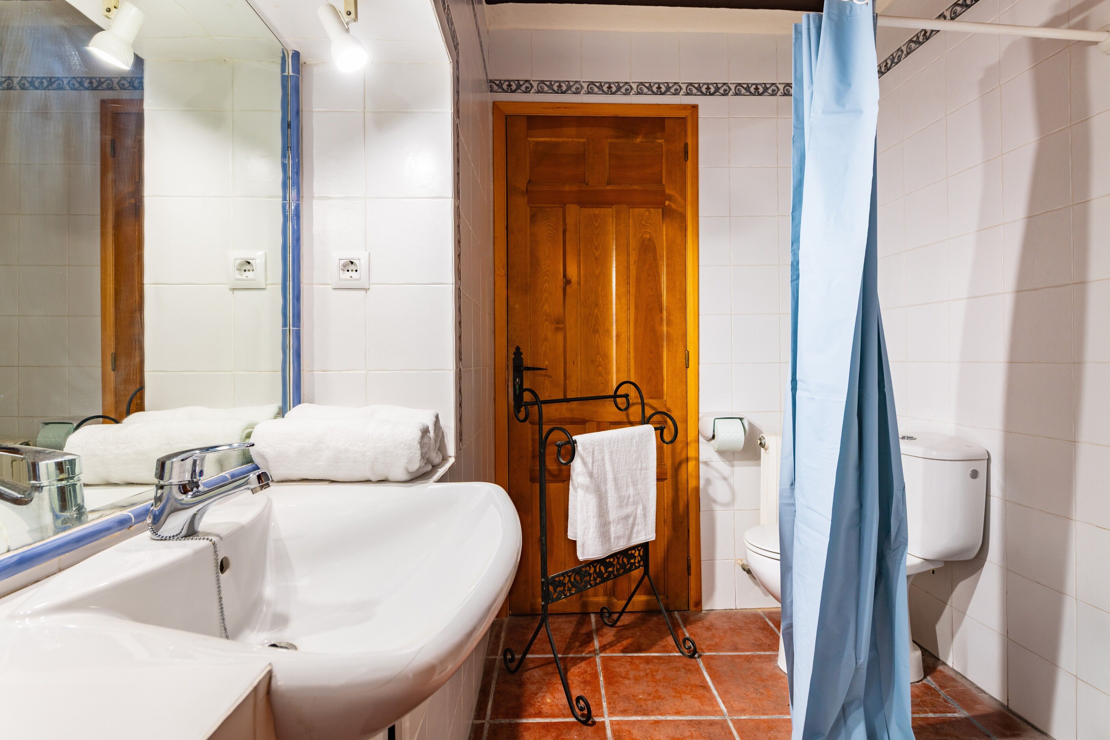 Un baño con lavamanos blanco, espejo y puerta de madera.