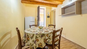 A dining area with a round table, chairs, a refrigerator, and a window with wooden shutters. - Holiday Home 'Zaami' with Sea View, Wi-Fi and Air Conditioning (Palermo)