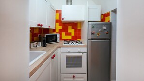 Een keuken met witte kastjes, een magnetron, een gasfornuis en een koelkast.