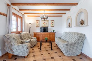 A living room with two patterned sofas, a wooden cabinet, a TV, and a chandelier. - Villa 'Merced' with Mountain View, Private Pool and Wi-Fi (Calpe)