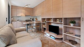 A modern living room with a sofa, TV, and built-in shelves. - Apartment 'Il Nido Del Lago' with Sea View, Wi-Fi and Air Conditioning (Colico Piano)
