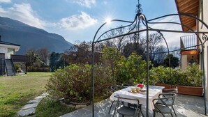 A patio with a table and chairs, surrounded by greenery and a mountain view. - Apartment 'Il Nido Del Lago' with Sea View, Wi-Fi and Air Conditioning (Colico Piano)