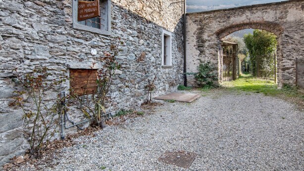 A stone building with a sign, a gravel path, and an arched gateway. - Apartment 'Il Nido Del Lago' with Sea View, Wi-Fi and Air Conditioning (Colico Piano)