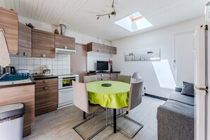 A modern kitchen with wooden cabinets, a dining table with chairs, a built-in oven, and a TV. - Charming 3★ house in Biscarrosse Plage – Shaded terrace, 300m from the ocean (Biscarrosse)