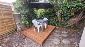 Eine Holzterrasse mit Tisch und Stühlen, umgeben von Grünpflanzen und einem Holzzaun.