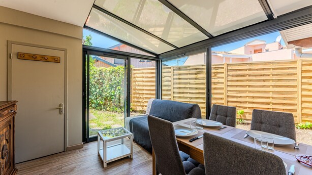 Een moderne kamer met glazen plafond, een eettafel gedekt voor vier personen, een bank en een houten kast.