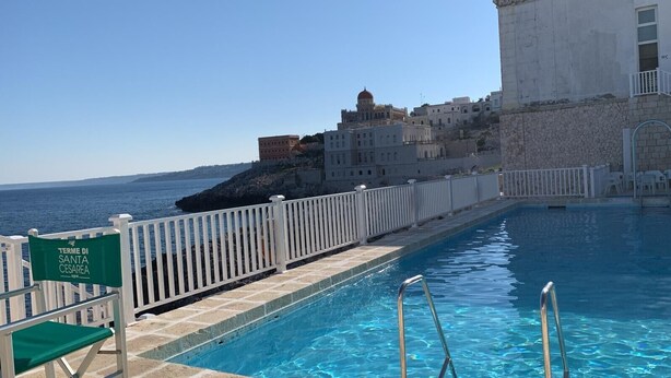 A swimming pool with a white fence, a sign for 'Termini di Santa Cesarea spa', and a building with a dome in the background. - Apartment 'I Due Soli' with Sea View, Wi-Fi and Air Conditioning (Santa Cesarea Terme)