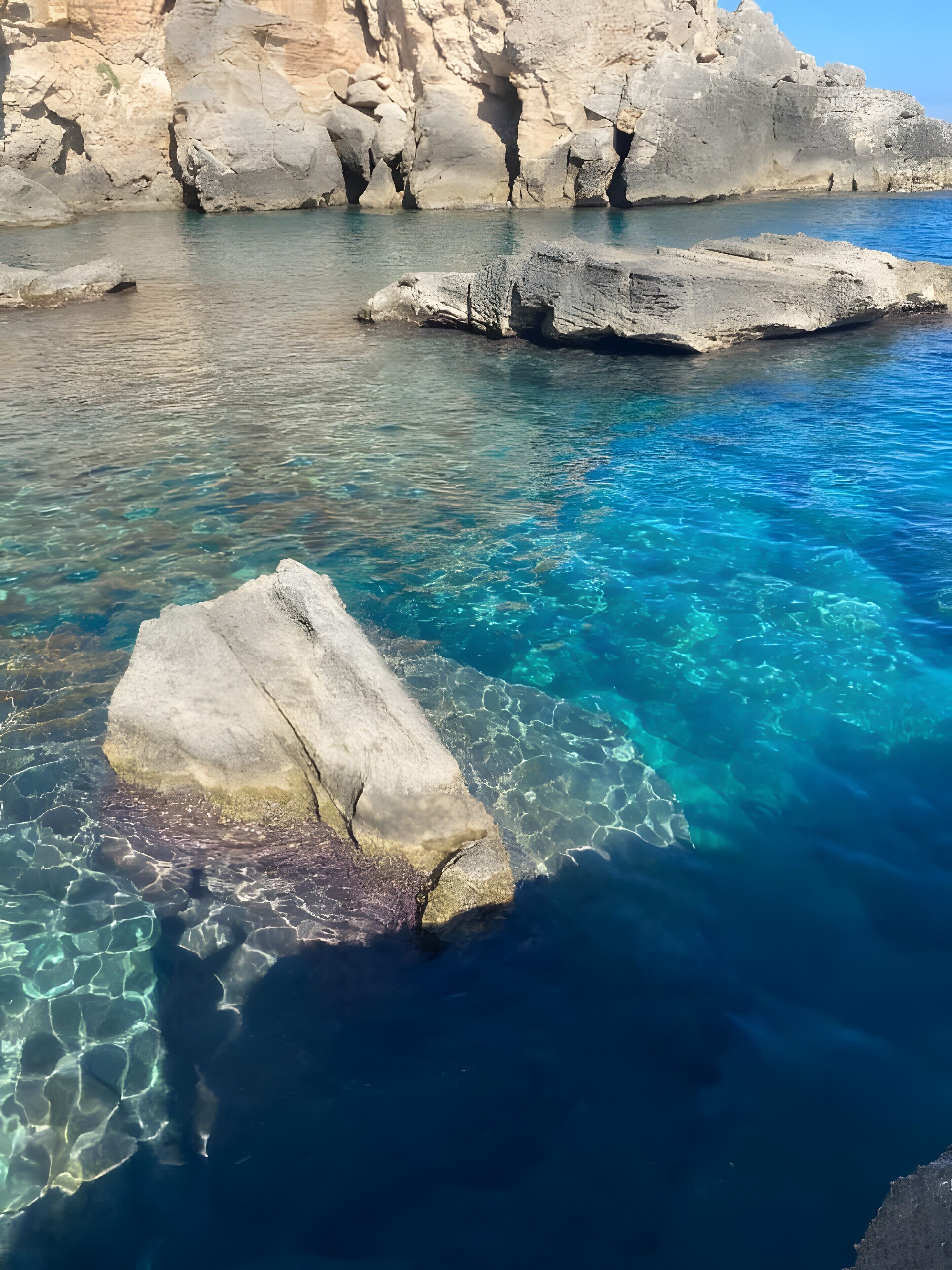 Une mer d’un bleu profond, parsemée de formations rocheuses, avec un grand rocher au premier plan.