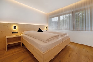 A modern bedroom with a wooden bed, bedside tables, and a large window with sheer curtains.