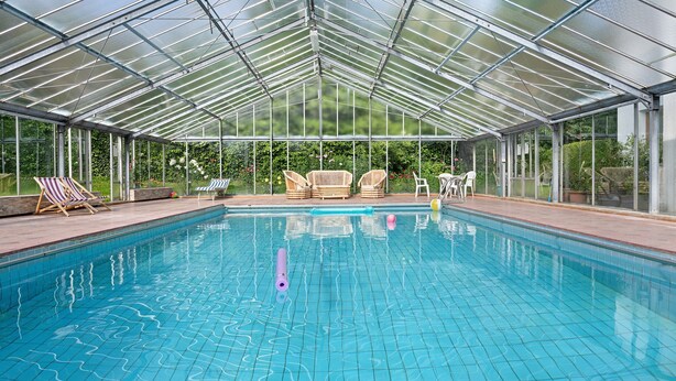 A covered swimming pool with clear blue water, surrounded by lounge chairs and a glass enclosure. - Holiday Apartment 'Klementhof No. 2' with Mountain View, Shared Pool and Wi-Fi (Naz-Sciaves)