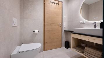 Et moderne badeværelse med dør i træ, et hvidt toilet, en vask med sort bordplade og et spejl.
