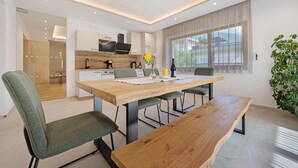 A modern dining area with a wooden table, green upholstered chairs, and a large window with sheer curtains. - Holiday Apartment 'Klementhof No. 2' with Mountain View, Shared Pool and Wi-Fi (Naz-Sciaves)