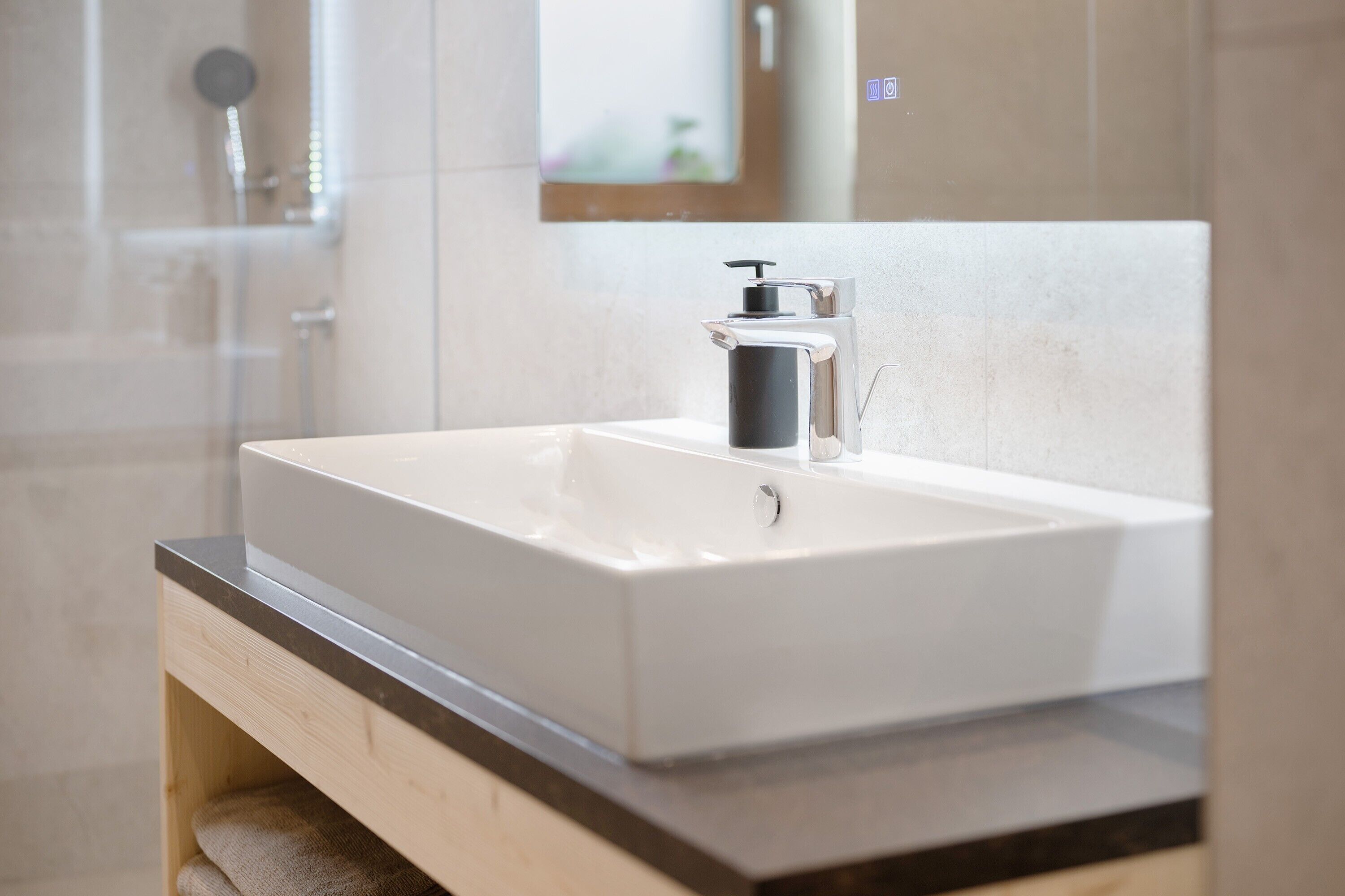 A bathroom with a white sink, a black soap dispenser, and a wooden vanity.