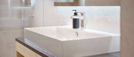 A bathroom with a white sink, a black soap dispenser, and a wooden vanity.