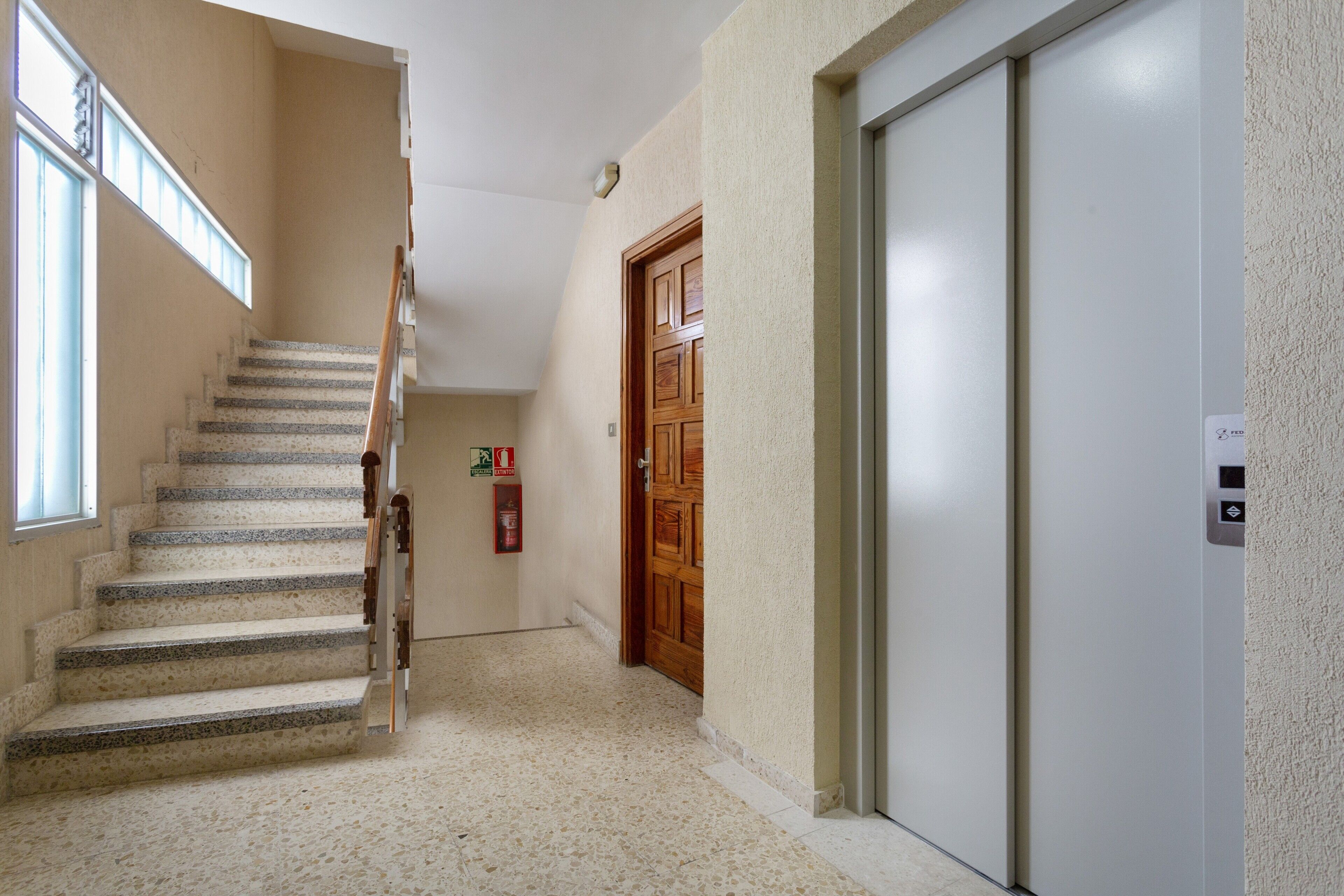 A hallway with a staircase, a wooden door, and a white elevator.