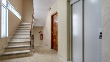 A hallway with a staircase, a wooden door, and a white elevator.