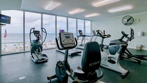 Ein Fitnessraum mit Cardiogeräten, Laufband und Ergometer mit Blick auf einen Strand.