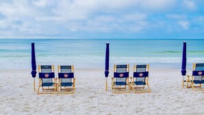 Ein Strand mit vier Liegestühlen und Sonnenschirmen, die in einer Reihe zum Meer ausgerichtet sind.
