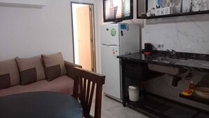 A compact living space with a kitchenette, a sofa, a dining table, and a TV mounted above the fridge.