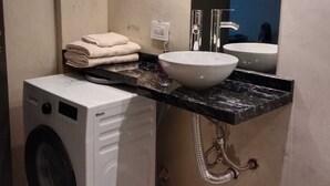 A bathroom with a washing machine, a sink, and a mirror.