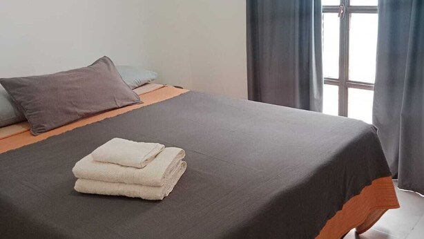A single bed with a grey and orange bedspread, a folded white towel, and a grey pillow.