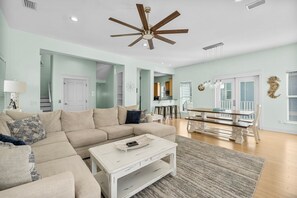 Un salon spacieux avec un canapé d’angle beige, une table basse blanche et un ventilateur de plafond.