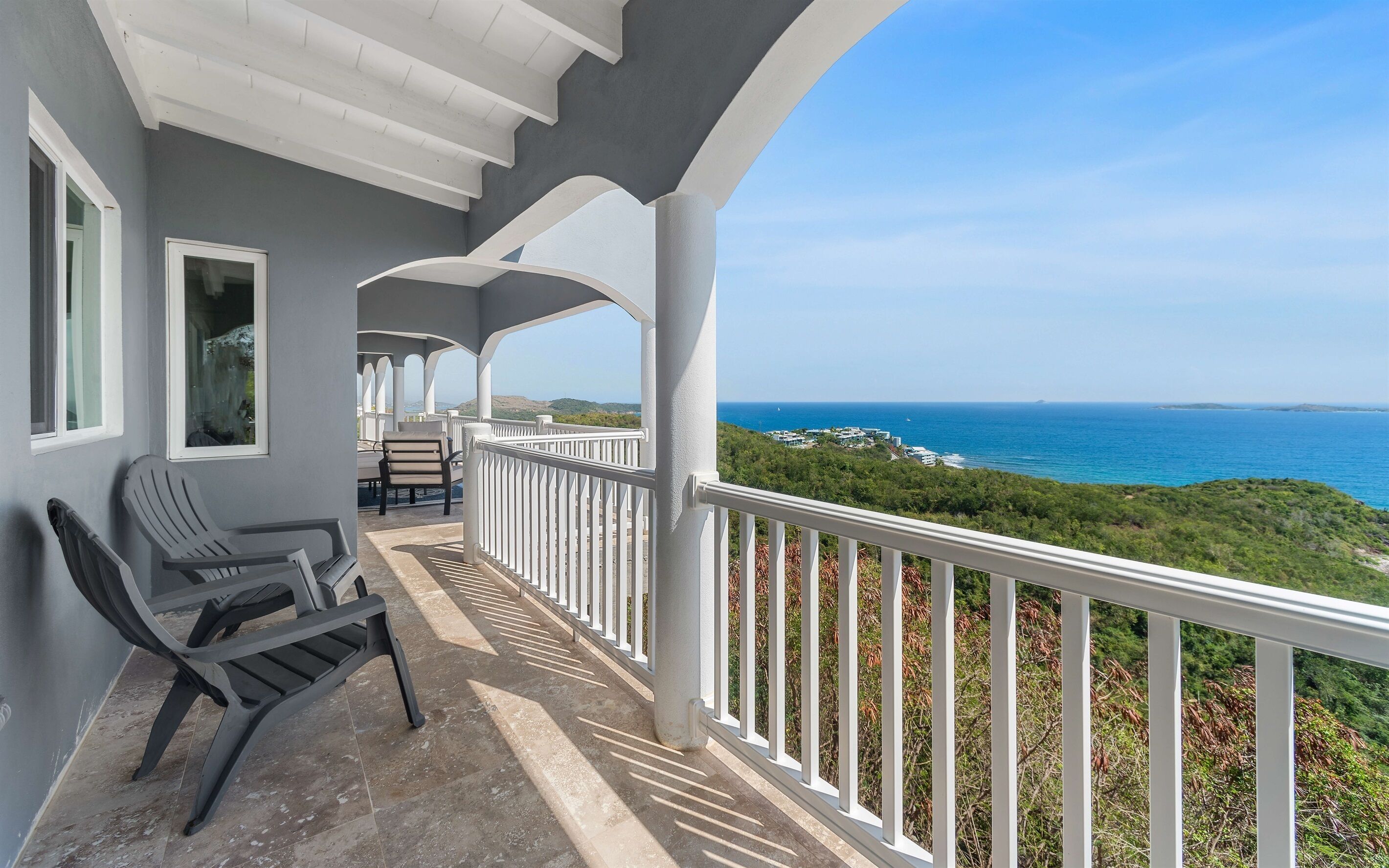 A balcony with a view of the ocean, a chair, and a table.