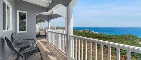 A balcony with a view of the ocean, a chair, and a table.