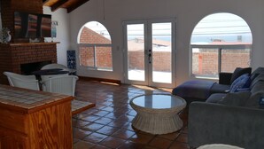 A spacious living area with a fireplace, a round table, and a couch. There are two large arched windows providing a view of the outside.