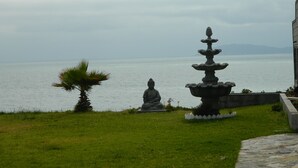 A serene outdoor area with a Buddha statue, a tiered fountain, and a view of the sea.