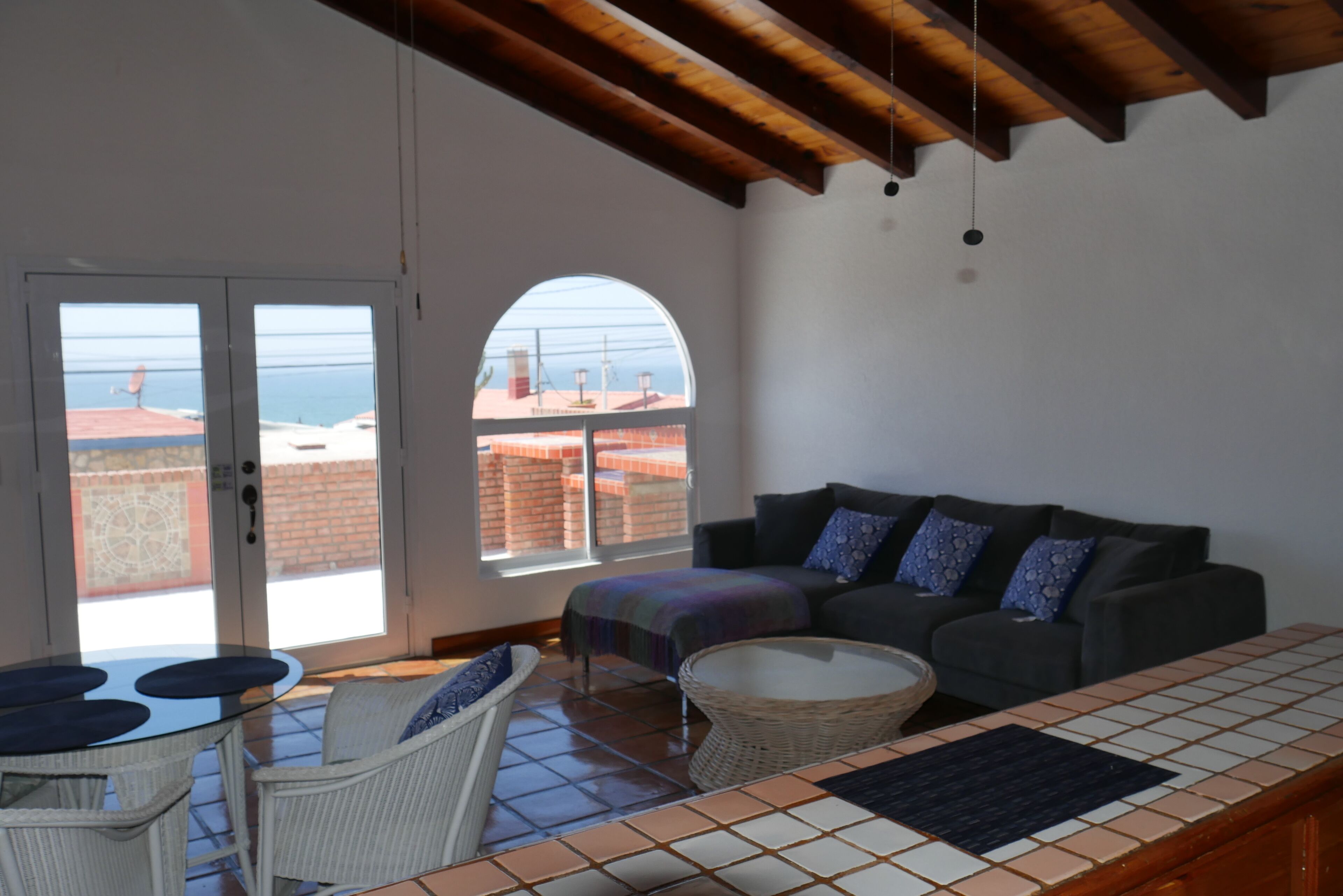 A spacious living area with a balcony, a sofa, a table, and a wicker chair.