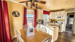 A kitchen with white cabinets, a wooden dining table, and a sign indicating coffee is served daily. - 2 Adjacent Houses Rented Together!! (Swanton)
