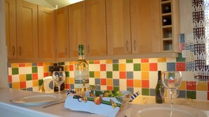 A kitchen with wooden cabinets, a colorful tiled backsplash, and a table set with plates, glasses, and a bottle of wine. - Appart 2 pièces 4 couchages PORT LEUCATE NATURISME (PORT LEUCATE NATURISME)