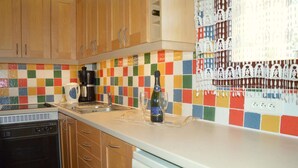 A kitchen with wooden cabinets, a colorful checkered backsplash, a coffee maker, a wine bottle, and a dishwasher. - Appart 2 pièces 4 couchages PORT LEUCATE NATURISME (PORT LEUCATE NATURISME)