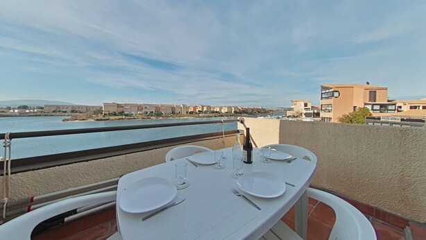 A dining table set for two with a view of the sea and buildings in the background. - Appart 2 pièces 4 couchages PORT LEUCATE NATURISME (PORT LEUCATE NATURISME)