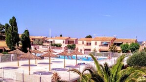 Ein Resort mit mehreren Gebäuden, einem Swimmingpool und strohgedeckten Sonnenschirmen.