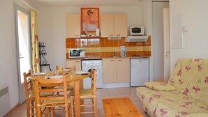 A compact kitchen with wooden cabinets, a microwave, a coffee maker, and a washing machine. - Mais 3 pièces 6 couchages PORT LEUCATE NATURISME (PORT LEUCATE NATURISME)
