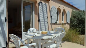 An outdoor dining area with a table and chairs, a basket, and a door leading to a room. - Mais 3 pièces 6 couchages PORT LEUCATE NATURISME (PORT LEUCATE NATURISME)