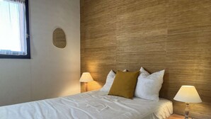 Ein ordentlich bezogenes Bett mit weißen Leinen und einem senfgelben Kissen, eingerahmt von zwei Nachttischlampen auf Holznachttischen.