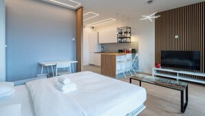 Moderni hotellihuone, jossa on suuri sänky, työpöytä, pieni keittiö ja televisio.
