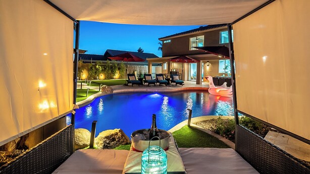 Vista de la piscina con un área de estar cubierta, sillas de descanso y un flotador con forma de cisne.